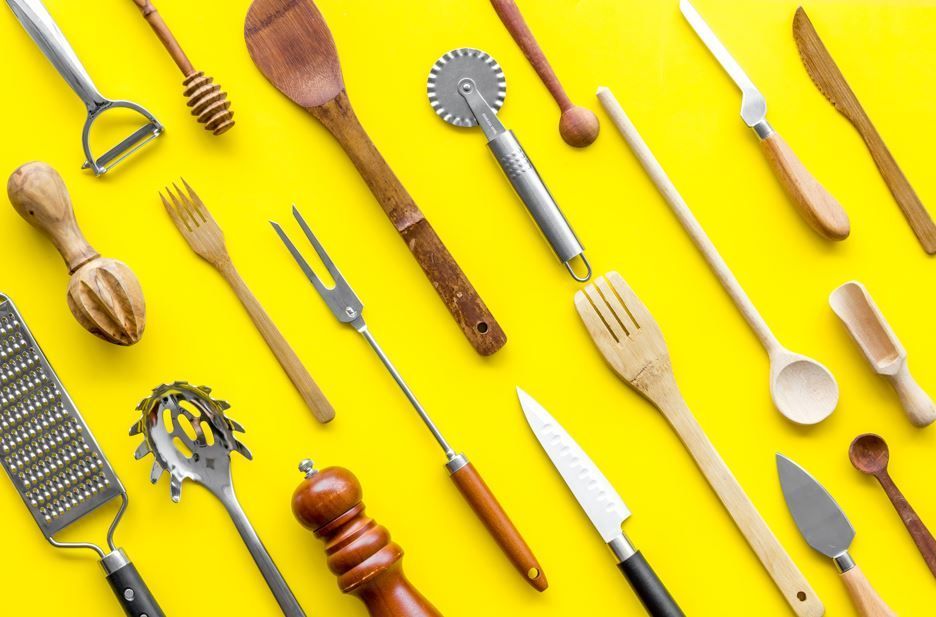 Utensilios de cocina sobre fondo amarillo. Incluye cucharas, cuchillos, ralladores y más.