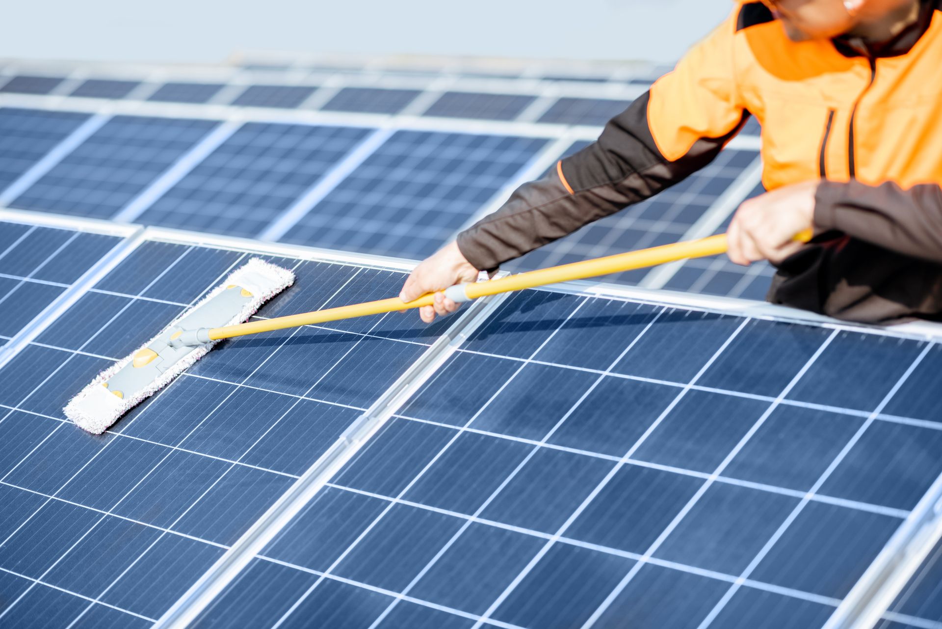 Ein Mann reinigt Solarmodule mit einem Mopp.