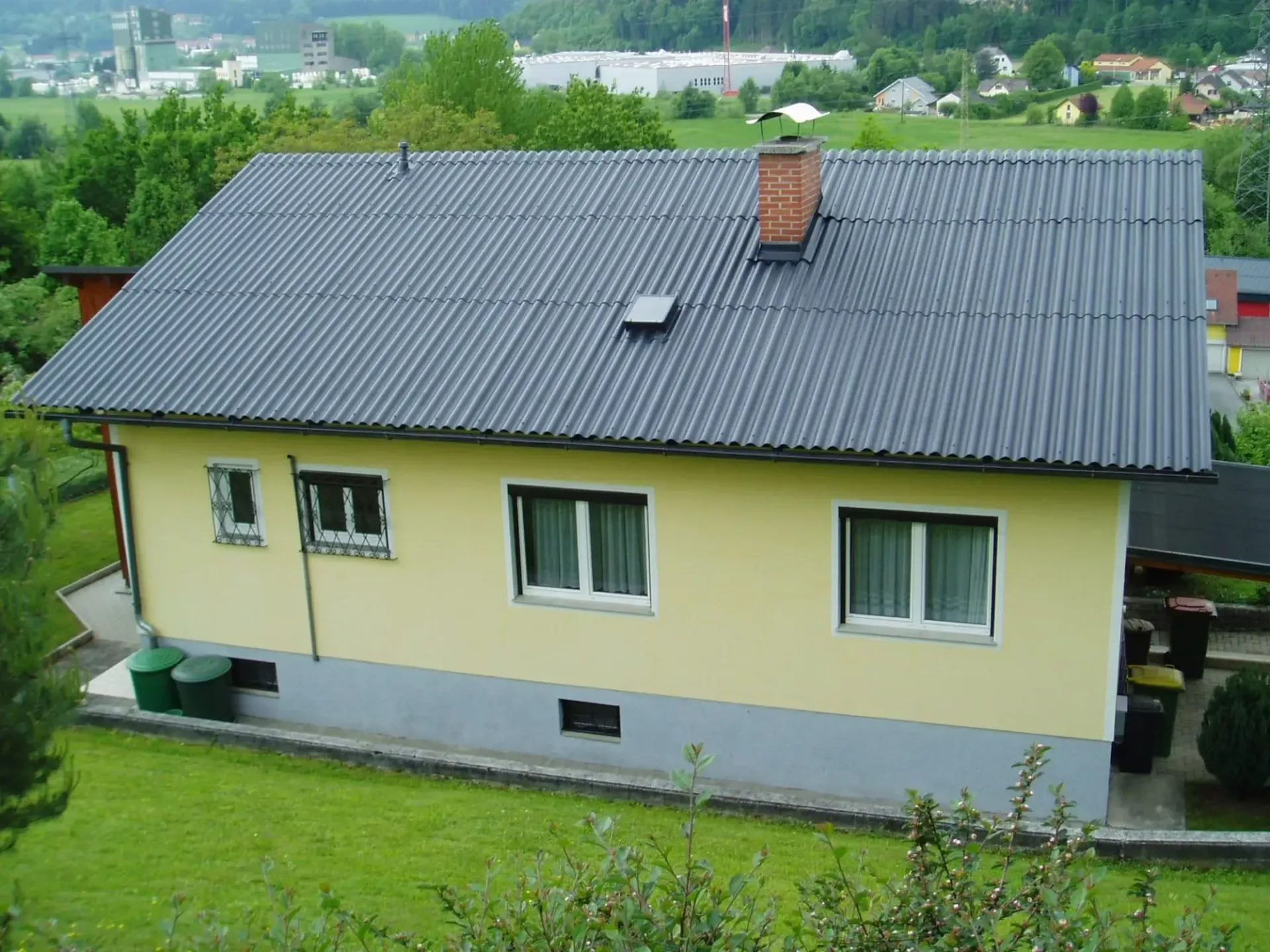 Ein gelbes Haus mit einem schwarzen Dach und einem Schornstein