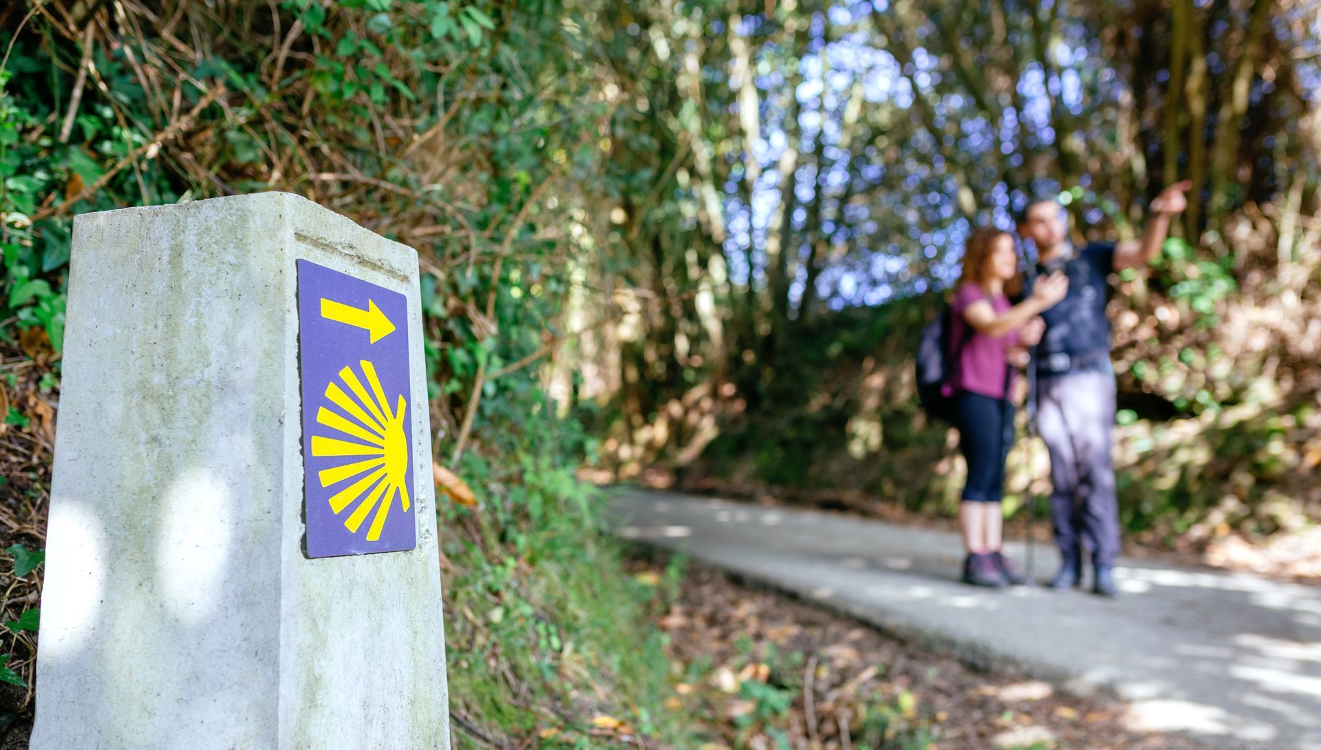 Un hombre y una mujer caminan por un sendero junto a un cartel de piedra.