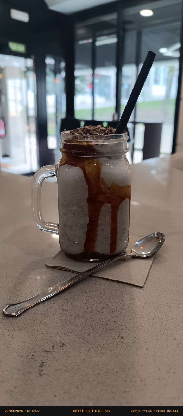Un batido en un frasco de vidrio con una cuchara y una pajita sobre una mesa.