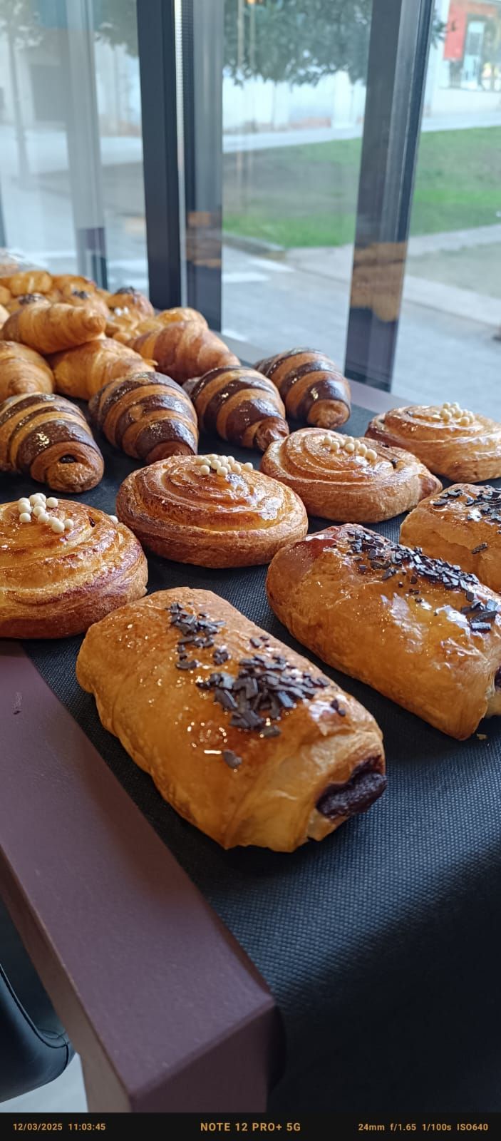 Un montón de pasteles están sobre una mesa frente a una ventana.