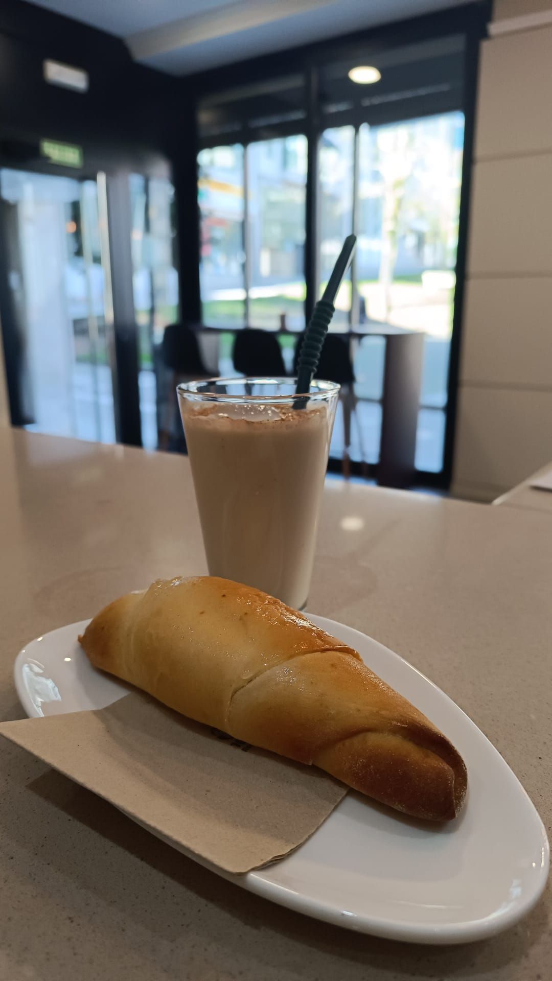 Hay un croissant y un batido en un plato sobre un mostrador.