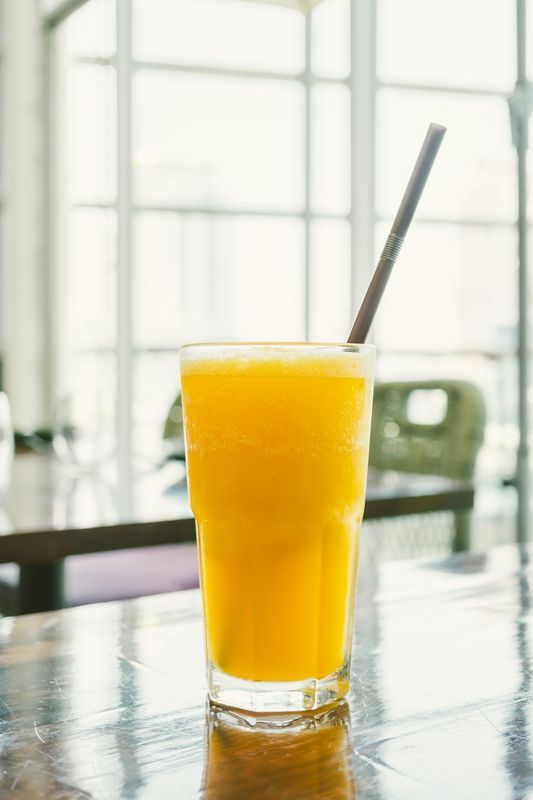 Un vaso de jugo de naranja con una pajita sobre una mesa de madera.