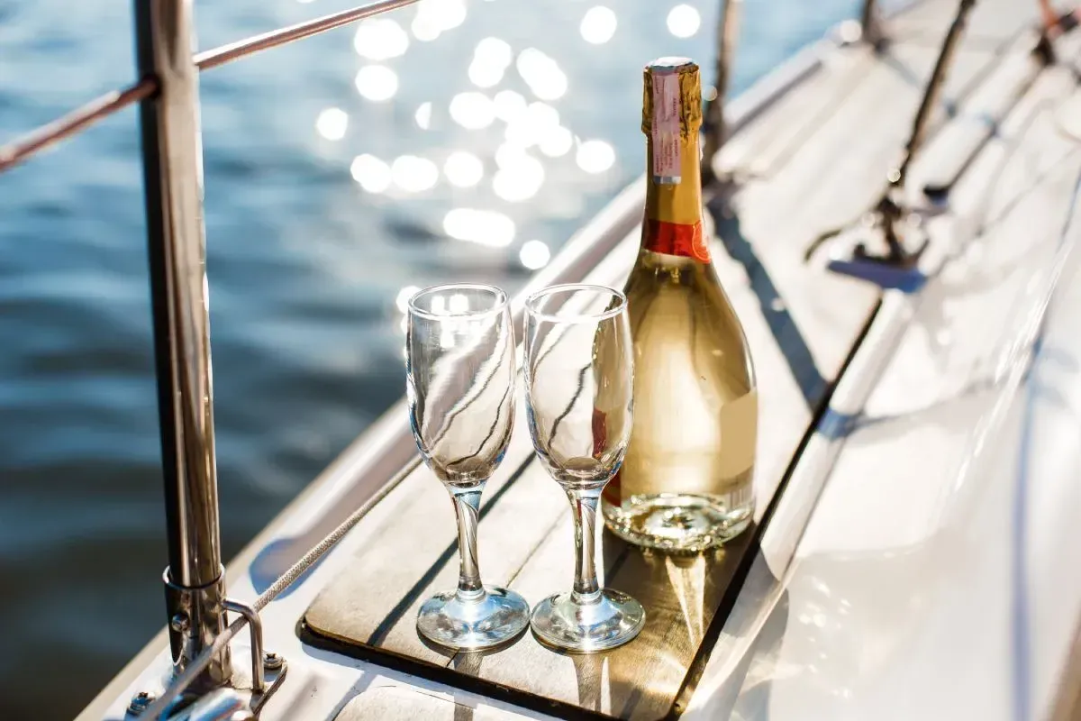 Champagne bottle and two glasses on a yacht, sparkling water in the background.