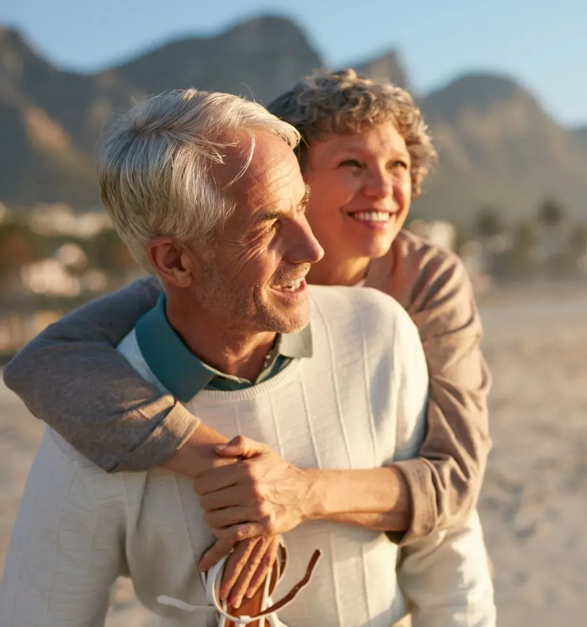 Couple embracing on a beach, smiling; mountains in background.