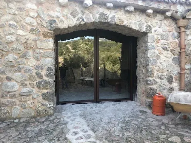 Entrada con muro de piedra y puertas de cristal oscuro que dan a un patio sombreado.