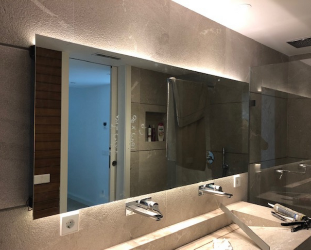 Baño moderno con un gran espejo de pared, lavabo doble y ducha a ras de suelo reflejada en el cristal.