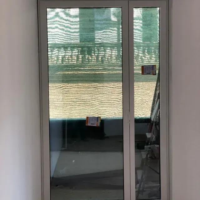 Puerta corrediza de cristal con una cortina de rayas verdes y una pequeña mesa visible en el interior.