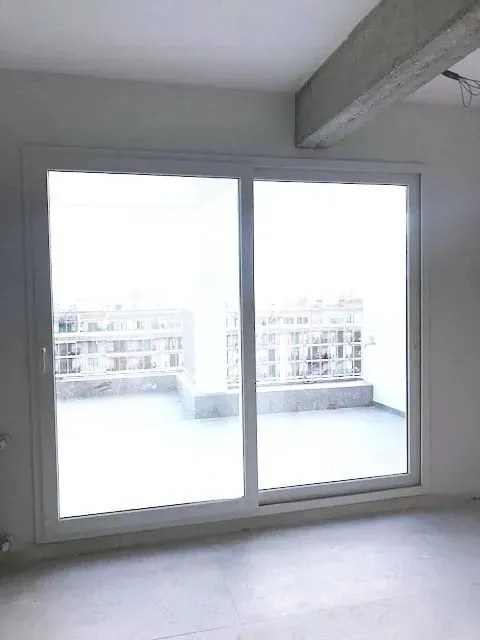 Habitación vacía en un apartamento con grandes puertas correderas de cristal que dan a un luminoso balcón con vistas.