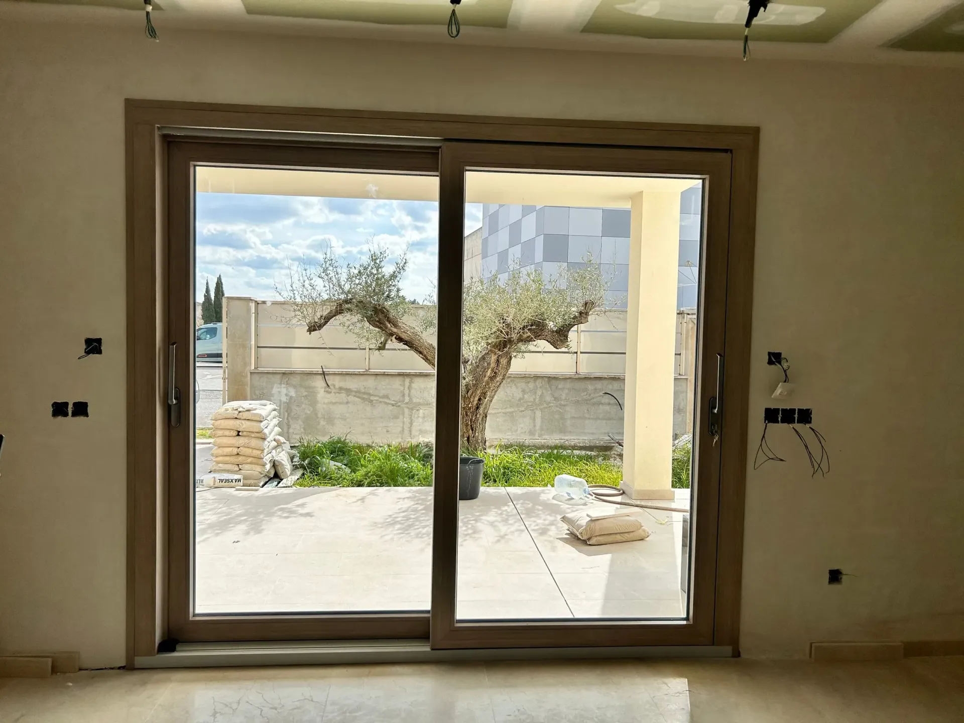 Habitación vacía con una puerta corredera de cristal que da a un patio con un árbol y un muro bajo.