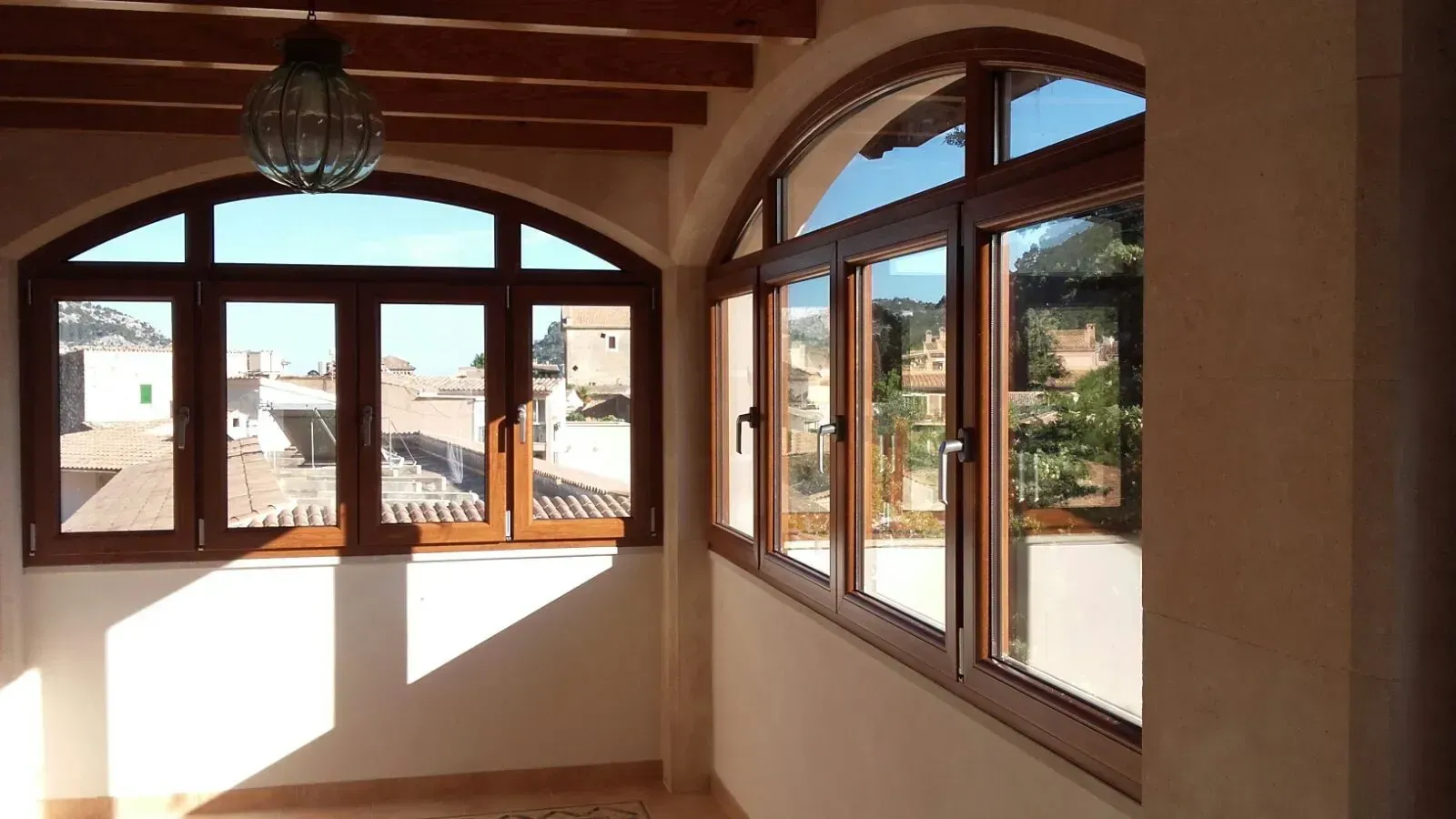 Habitación luminosa con ventanas arqueadas, vigas de madera y luz solar que inunda el suelo.
