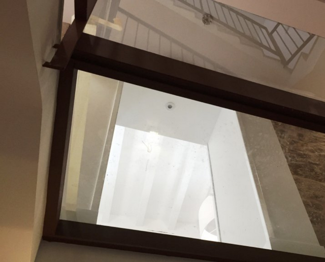Vista de una escalera con paredes beige, barandillas oscuras y un suelo blanco.