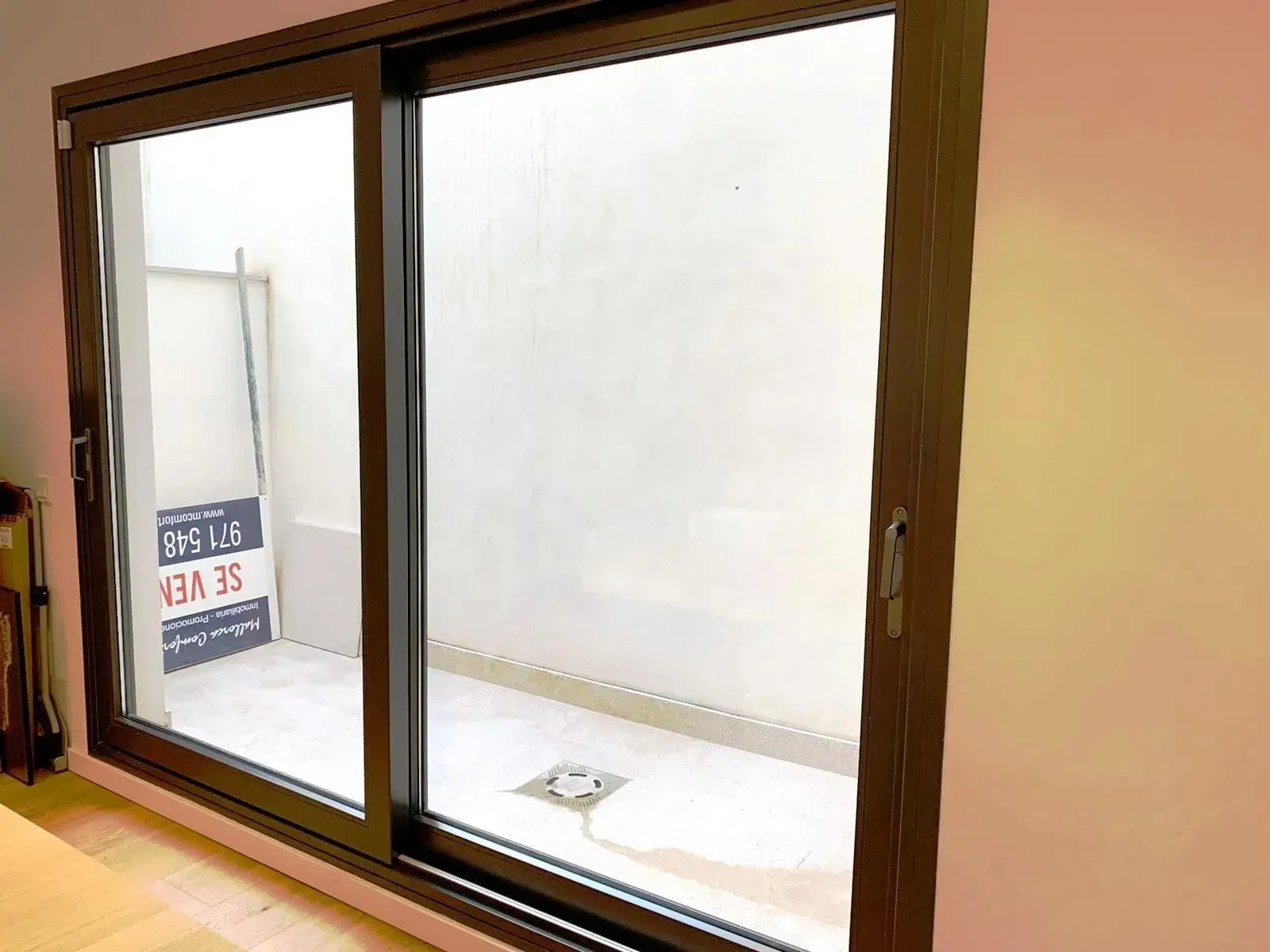 Puertas corredizas de cristal que dan a un pequeño patio blanco con un letrero a la izquierda.