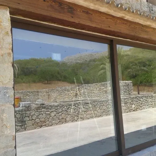 Ventana reflectante en un edificio de piedra, que muestra una ladera y un muro de piedra en el exterior.