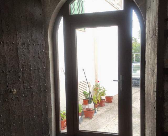 Un arco de entrada enmarca un luminoso patio exterior con macetas y una barandilla.