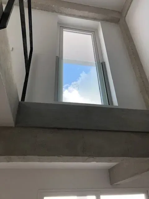 Vista desde una escalera hacia una ventana estrecha que muestra cielo azul y nubes.
