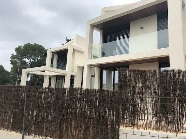 Casas blancas modernas con balcones detrás de una alta valla oscura tejida en el exterior.