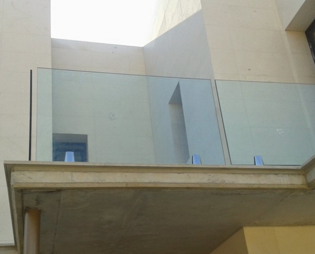 Interior de un edificio moderno con barandillas de balcón de cristal y paredes beige, visto desde abajo.