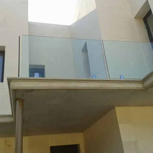 Balcón de un edificio moderno con barandilla de cristal y paredes de color beige, visto desde abajo.