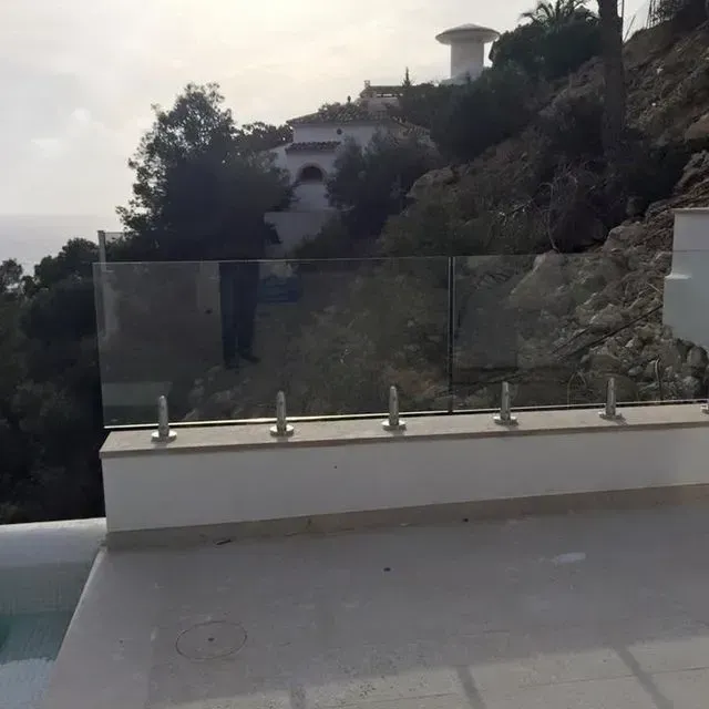 Terraza moderna con barandilla de cristal con vistas a una ladera rocosa y árboles al atardecer.