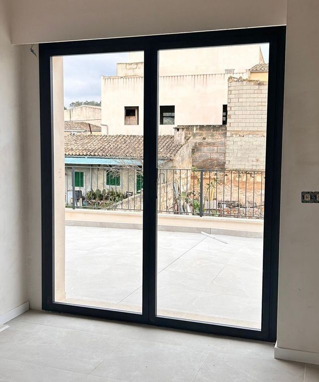 Habitación vacía con puertas corredizas de cristal con marcos negros que dan a una calle y a los edificios del exterior.