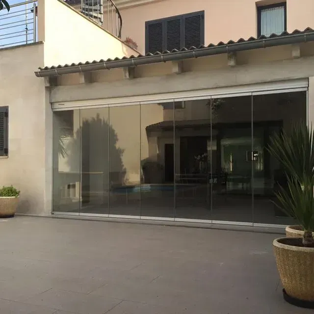 Patio moderno con escaparate de cristal, paredes beige, plantas en macetas y un patio embaldosado.