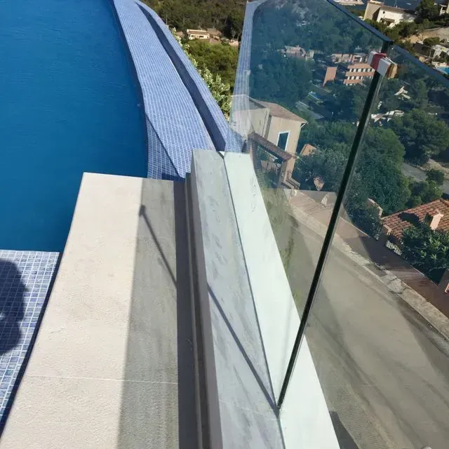 Balcón de cristal con vistas a una piscina azul y a los edificios de la ladera.