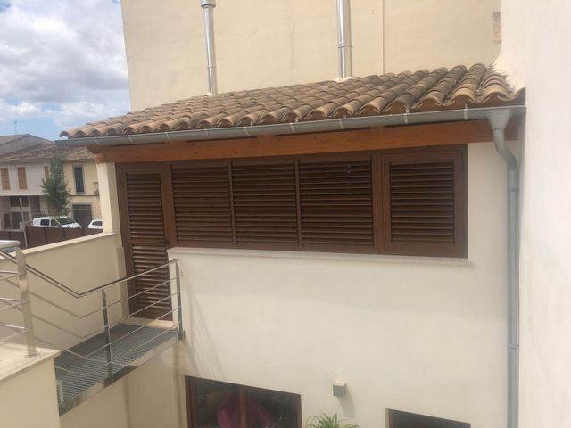 Exterior de un edificio beige con contraventanas marrones y un tejado de tejas sobre una escalera con balcón.