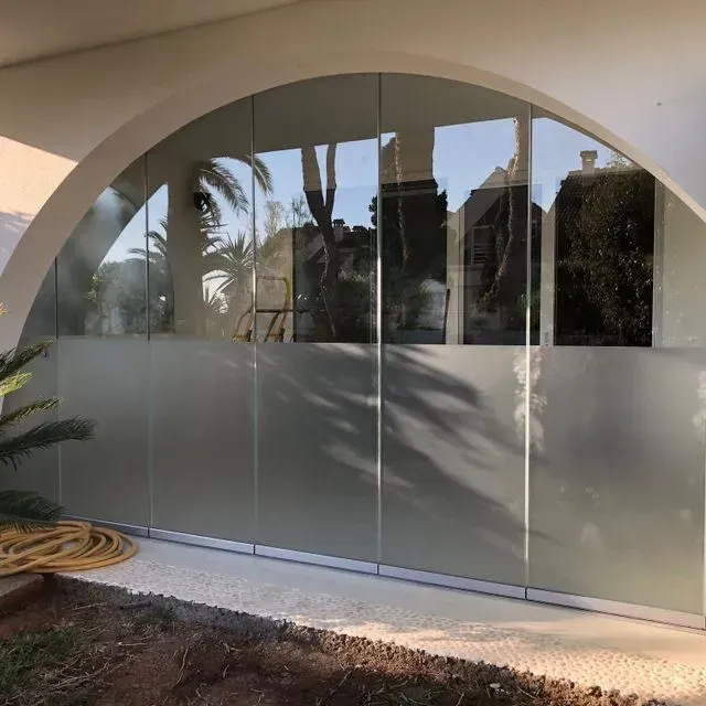 Puertas arqueadas de cristal esmerilado que reflejan palmeras y un jardín.