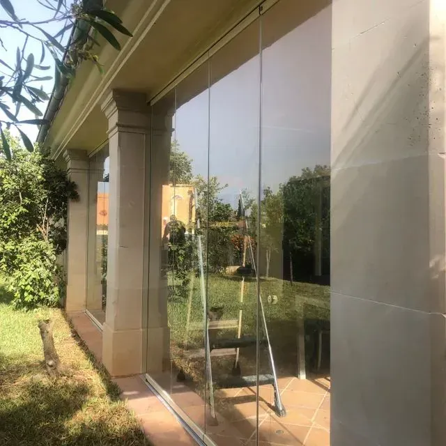 Pared de cristal en el patio con cuerdas colgantes junto a un jardín y césped bañados por el sol.
