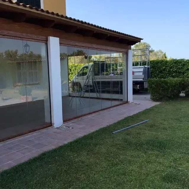 Patio con pared de cristal, sendero de baldosas, césped, seto y un camión de servicios públicos estacionado al fondo.