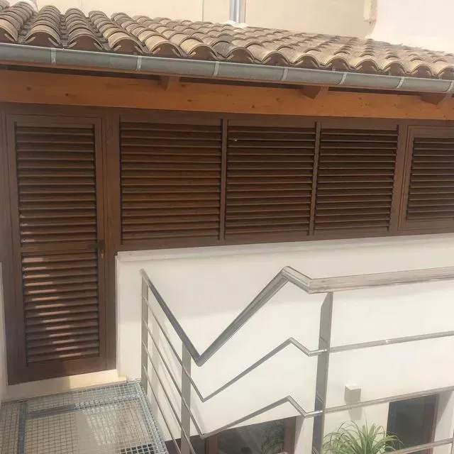 Escalera exterior junto a un edificio de estuco blanco con contraventanas marrones y tejado de tejas.