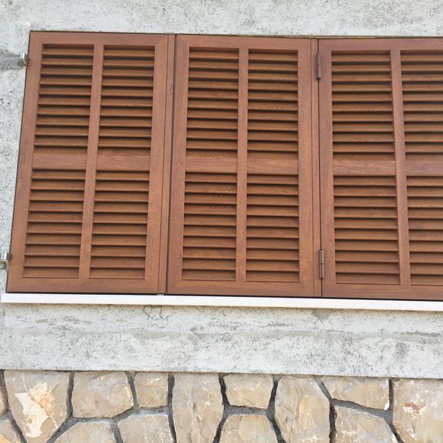 Persianas de madera marrón en la pared de una casa sobre una base de piedra.