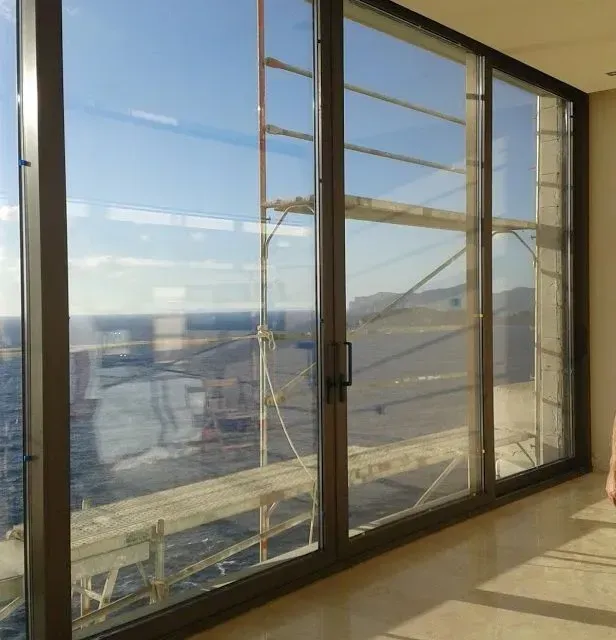 Balcón soleado con puertas de cristal del suelo al techo con vistas al océano y a una costa lejana.