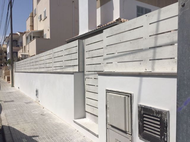 Acera residencial junto a un muro de listones blancos y una puerta a lo largo de un edificio de apartamentos.