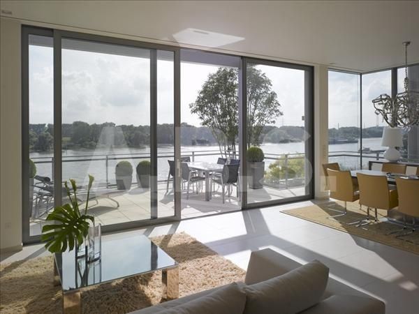 Luminoso salón moderno con ventanales del suelo al techo con vistas a un lago y a un comedor en el patio.