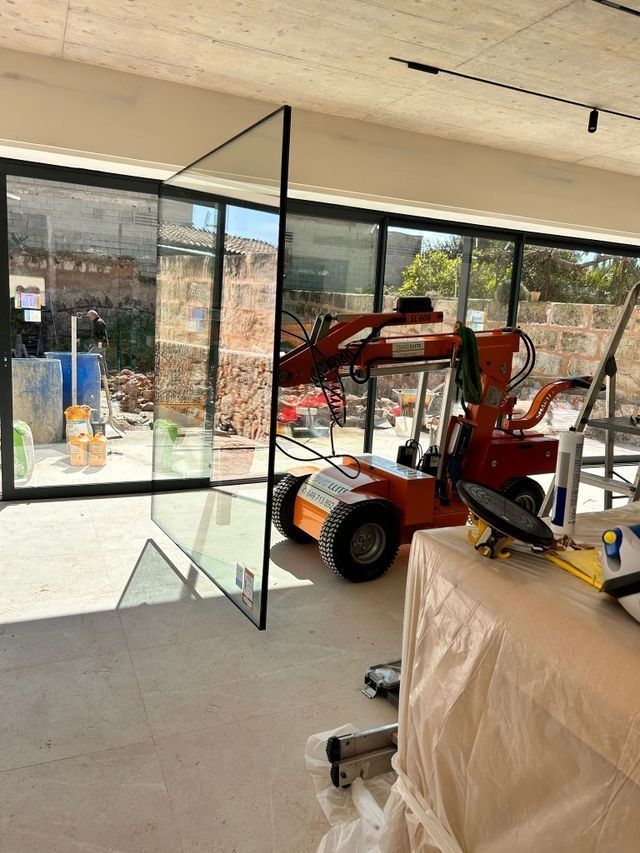Una carretilla elevadora naranja dentro de una habitación con paredes de cristal, con herramientas y muebles cubiertos cerca.