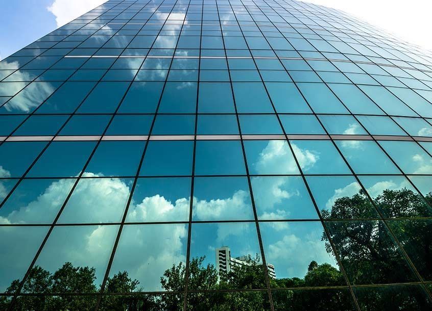 Edificio de oficinas de cristal que refleja el cielo azul, las nubes y los árboles.