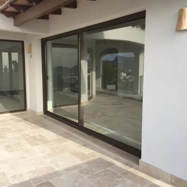 Patio cubierto con grandes puertas corredizas de vidrio y piso de baldosas en una casa moderna.