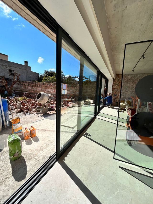 Habitación luminosa y moderna con puertas de cristal que van desde el suelo hasta el techo, con vistas a una soleada obra en construcción y al cielo azul.