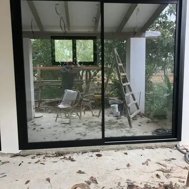 Unas puertas corredizas de cristal dan a un patio con una silla, una escalera, un cubo y hojas esparcidas.