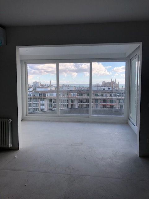 Habitación vacía con grandes ventanales que dan al horizonte de la ciudad al atardecer.