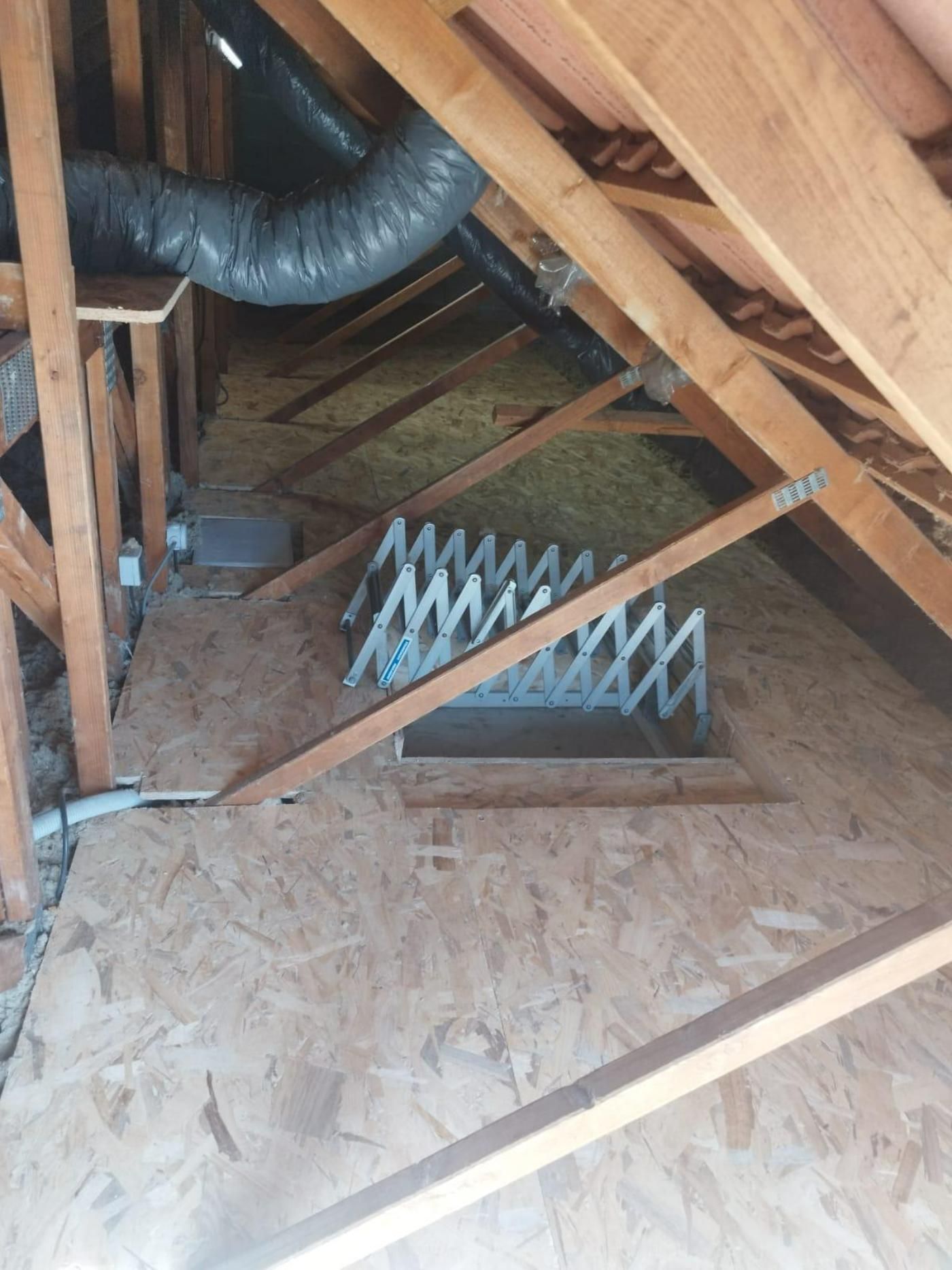 Intérieur mansardé avec poutres en bois, trappe et dispositif métallique de type accordéon.