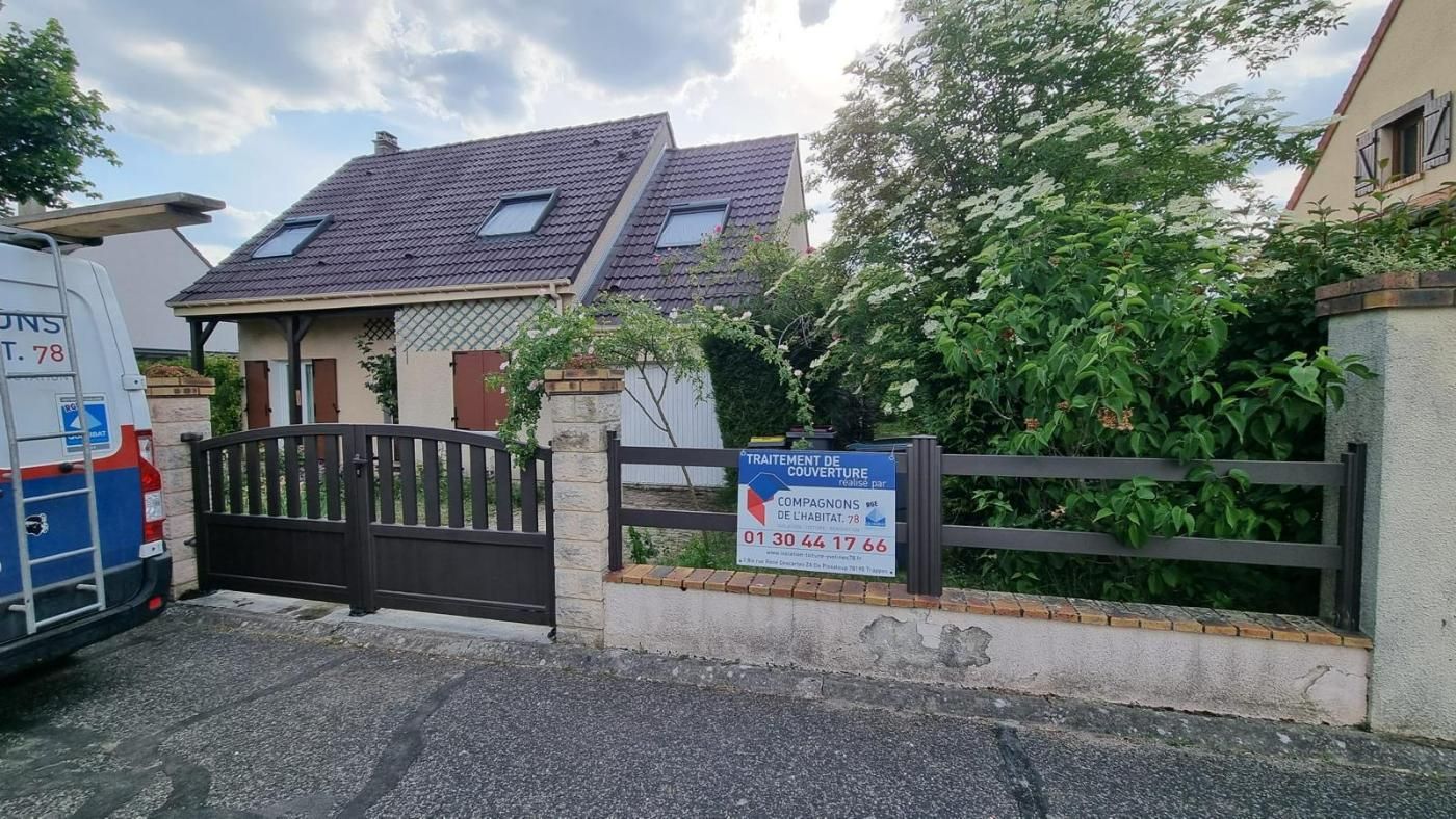 Maison marron fermée avec clôture marron et mur de briques, arbre.