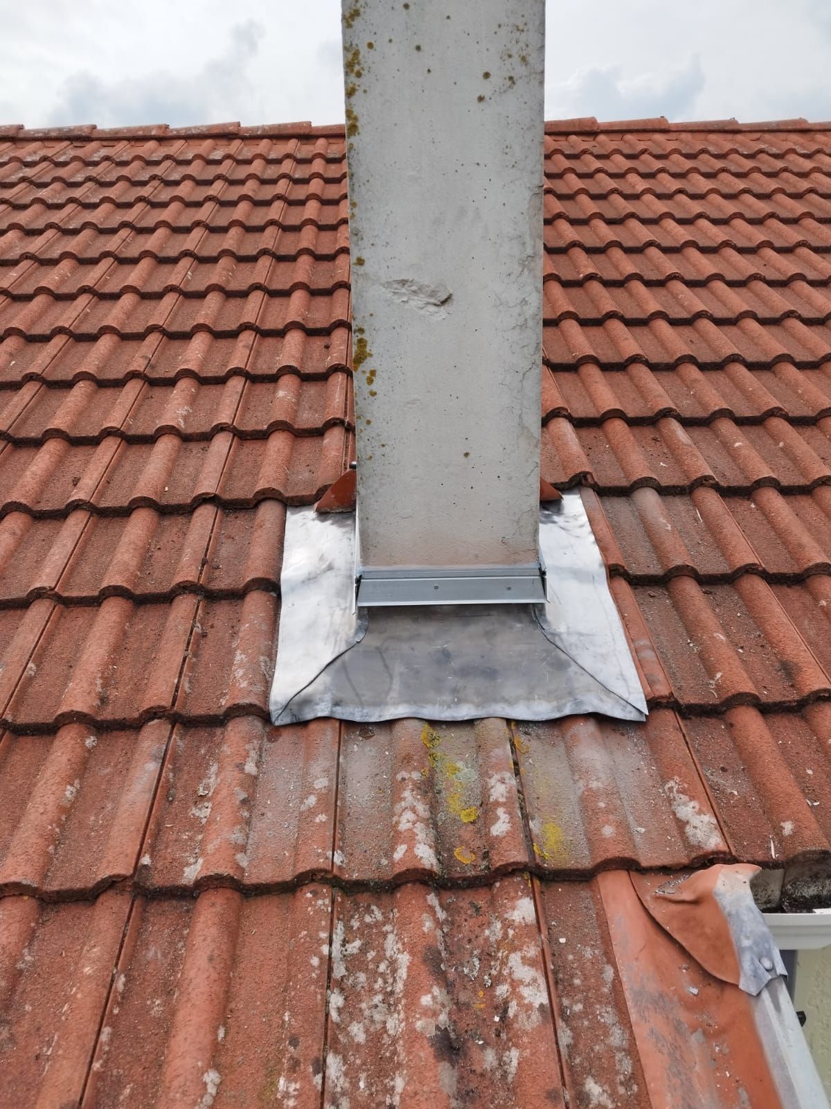 Cheminée métallique émergeant d'un toit de tuiles rouges avec solins en plomb