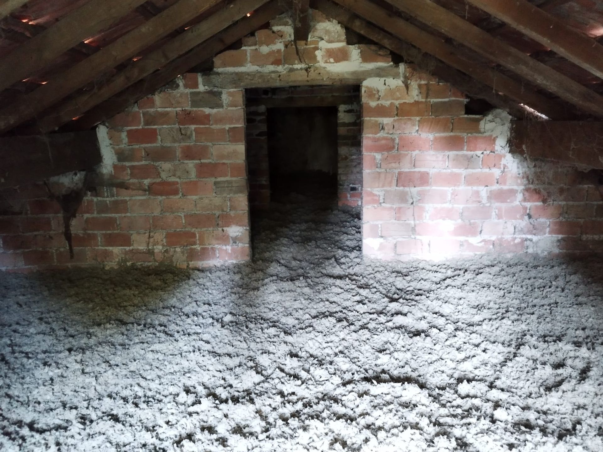 Intérieur d'un grenier avec des murs en briques et une porte, rempli d'isolant