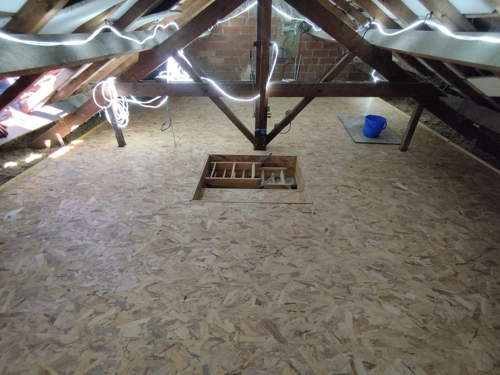 Intérieur du grenier avec plancher en contreplaqué, poutres en bois, éclairage au plafond et trappe d'accès