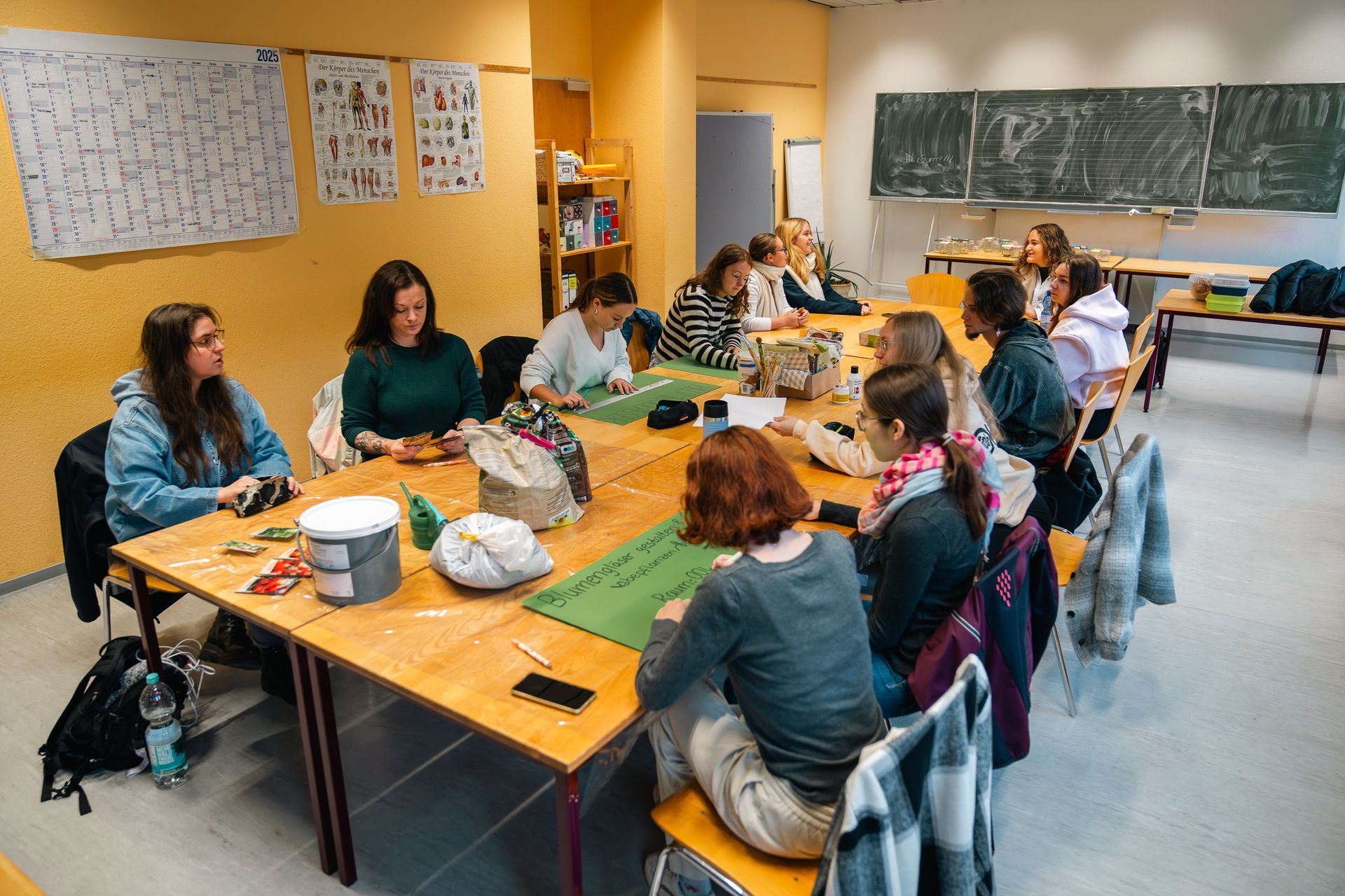 Eine Gruppe von Menschen sitzt an einem Tisch und bastelt in einem Raum mit einer Tafel.