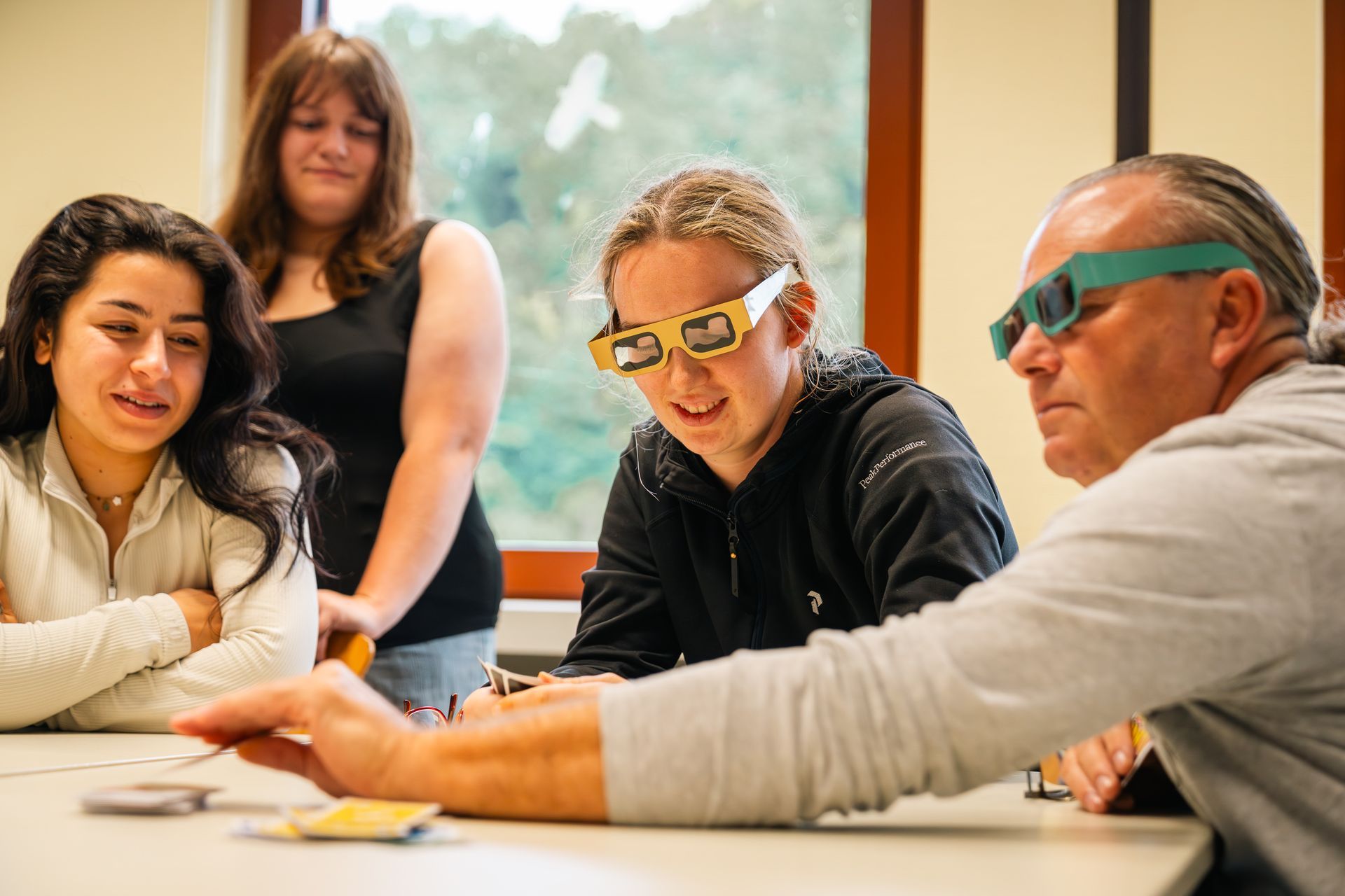 Vier Personen sitzen an einem Tisch; eine trägt eine 3D-Brille. Sie betrachten Gegenstände, vermutlich in einem Bildungskontext.